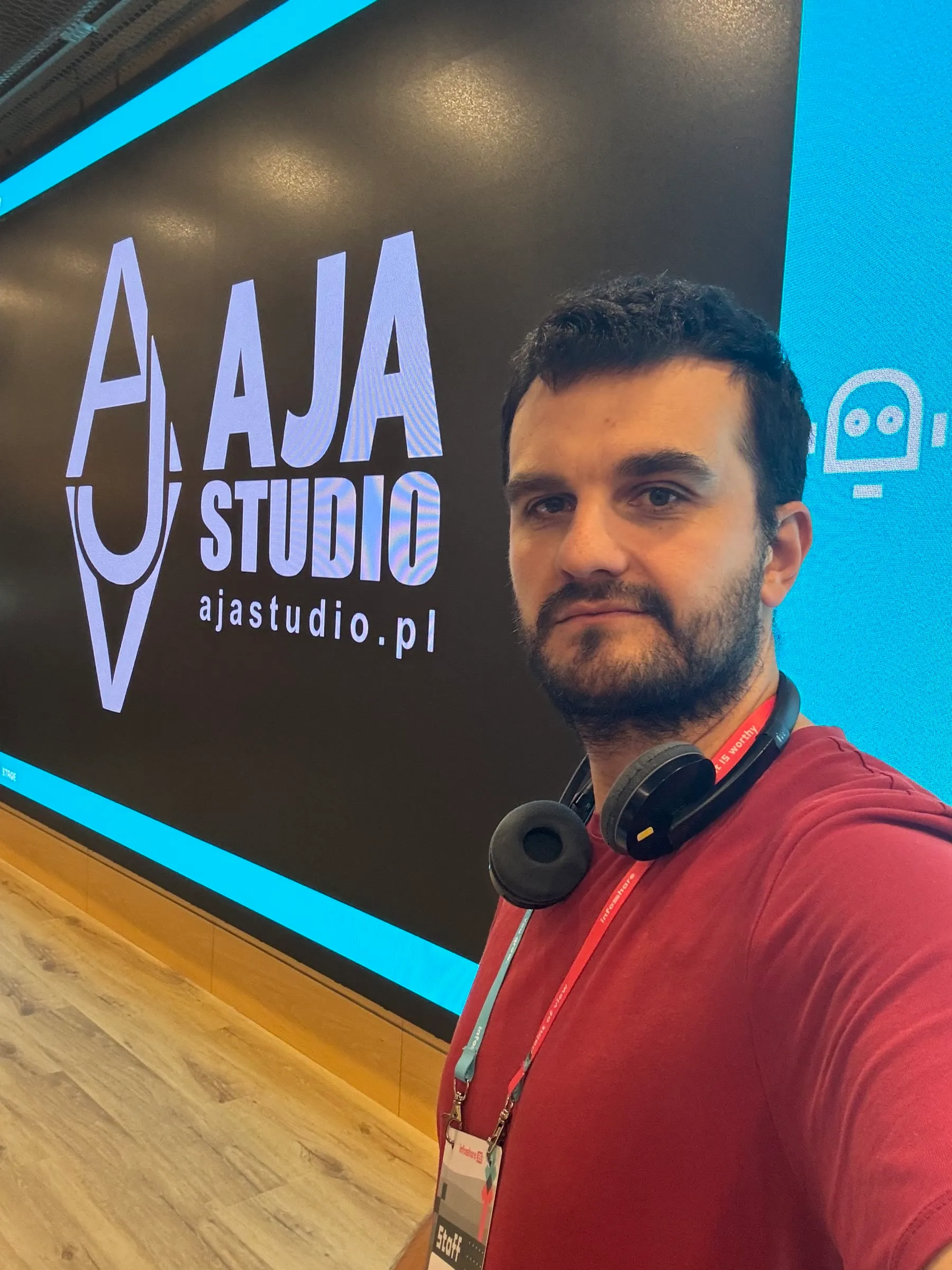 Adrian Jerzy Amrugiewicz w słuchawkach przed ekranem z logo AJA Studio