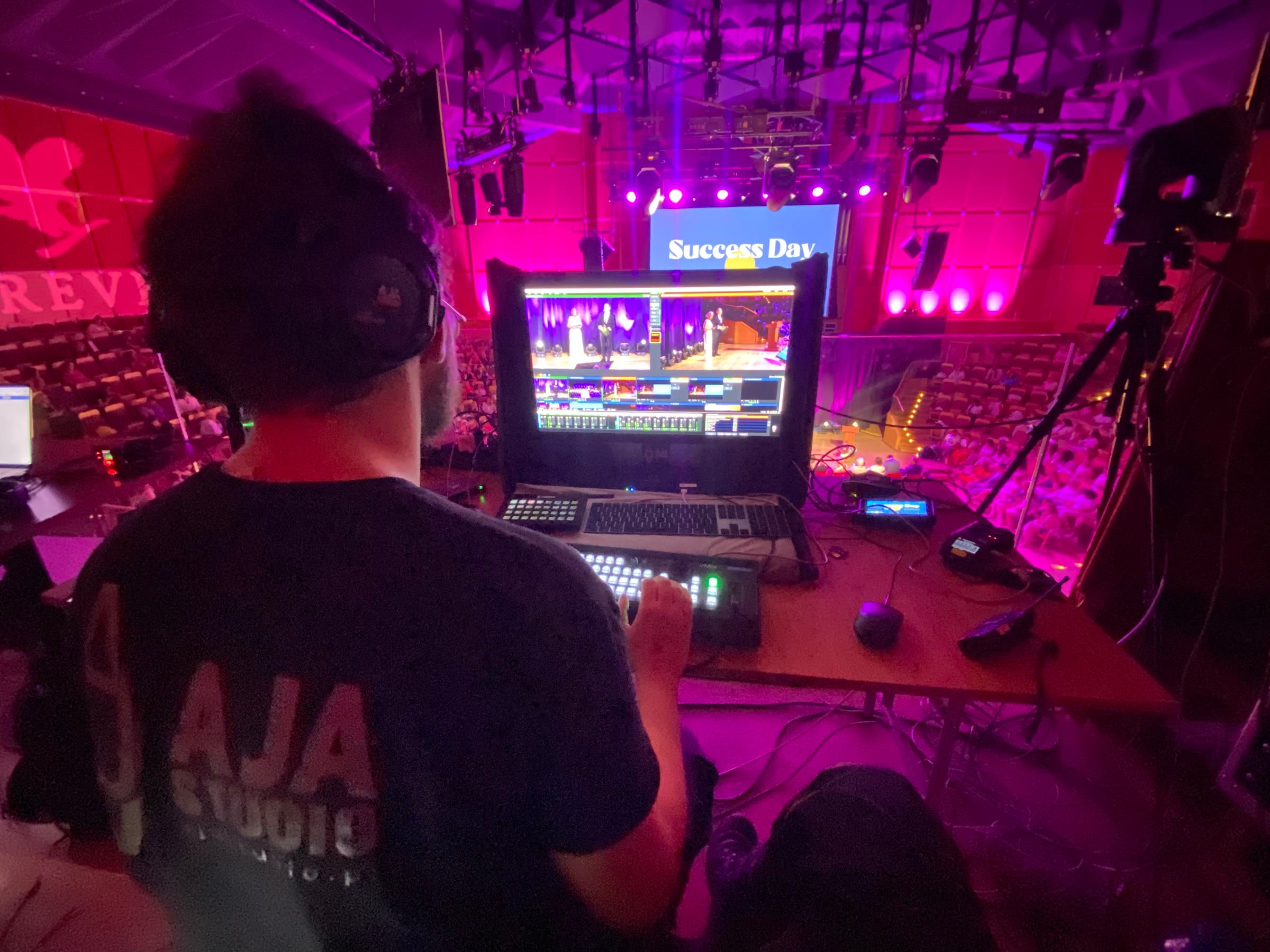 Realizator AJA Studio przy stanowisku realizacji wielokamerowej z widokiem na scenę i publiczność