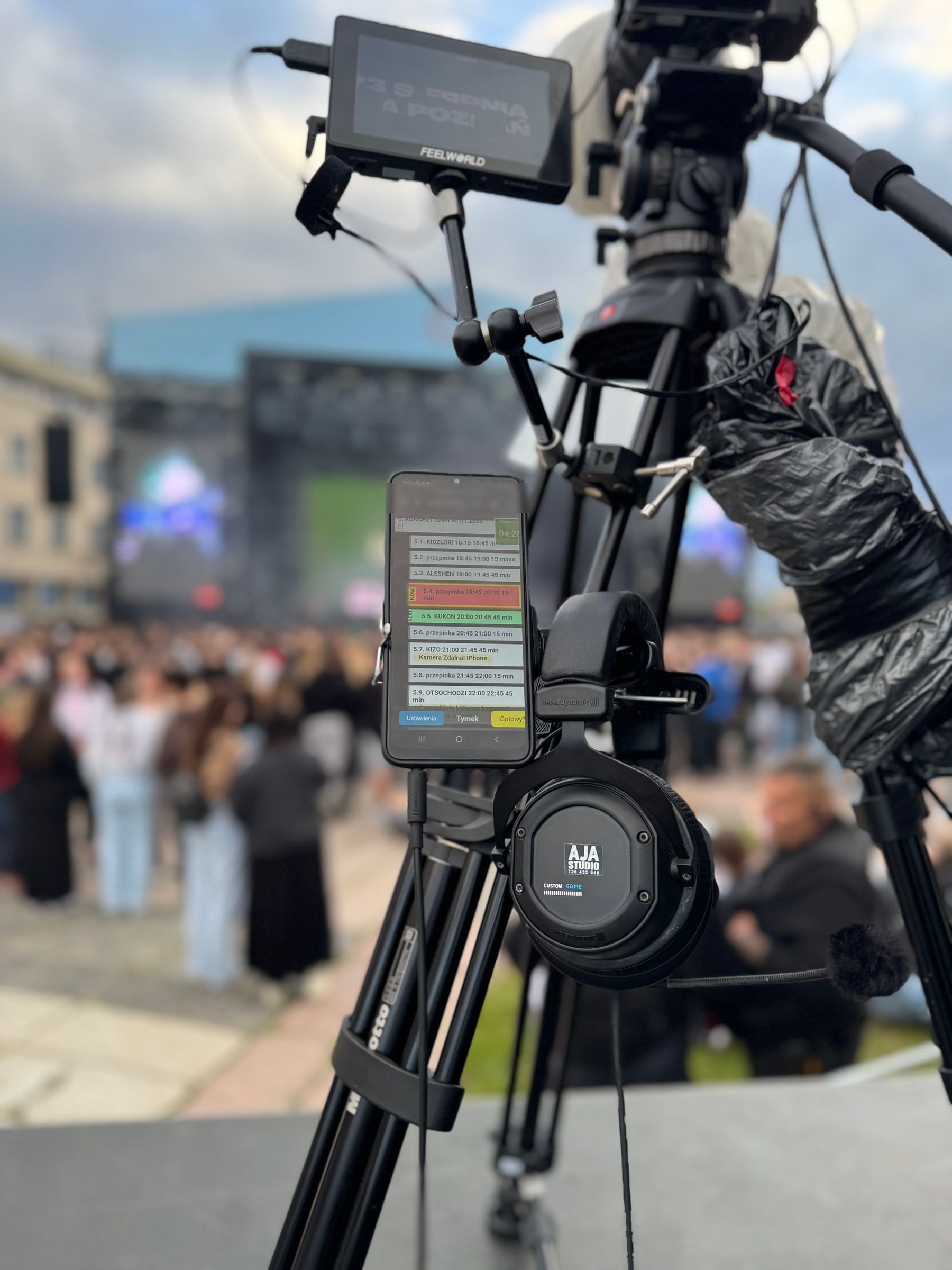 Stanowisko kamery na plenerowym wydarzeniu: monitor, telefon z AJA Skrypt i słuchawki AJA Studio, w tle publiczność i scena